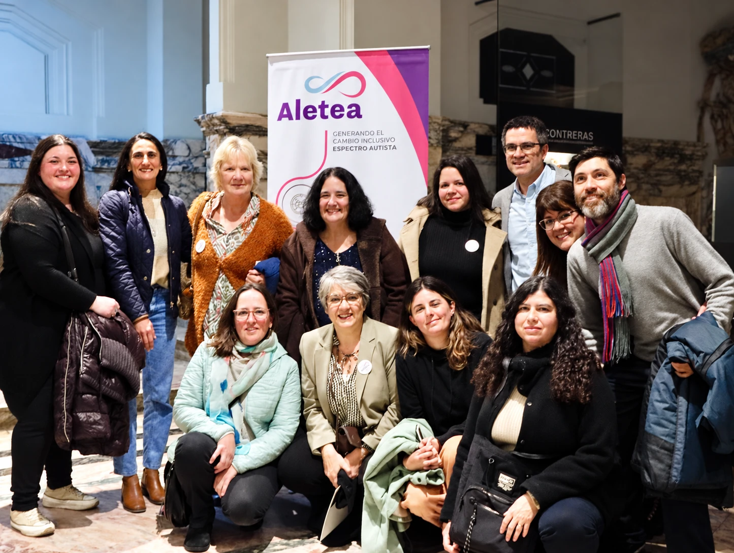 Personas posan junto a un cartel de Aletea en un espacio interior.