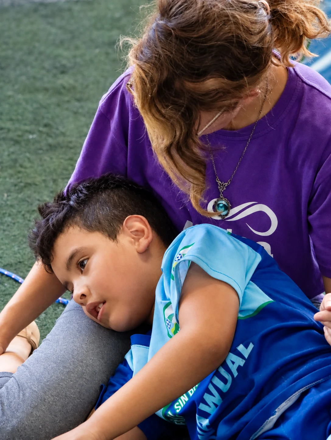 Un niño apoya la cabeza en el regazo de una persona con camiseta violeta.